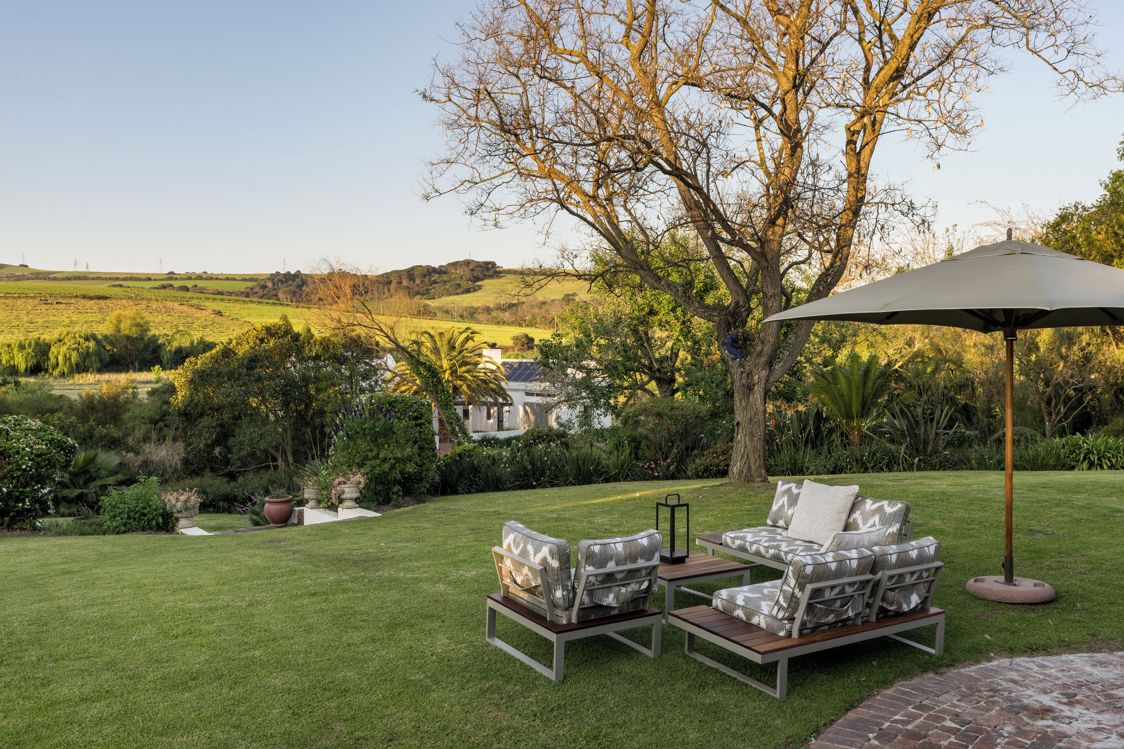 A patio with outdoor furniture, a tree, and a view of a house and landscape.