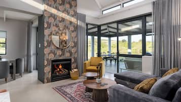 A modern living room with a fireplace, a sofa, a coffee table, and a view of the outdoors.