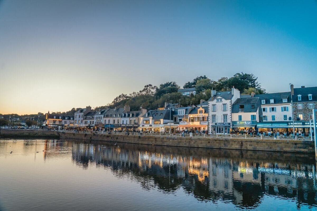 A waterfront promenade with buildings, shops, and a calm river reflecting the structures.