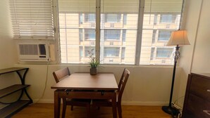 Une pièce comprenant une table à manger en bois, des chaises, une plante en pot, un lampadaire et un appareil de climatisation.
