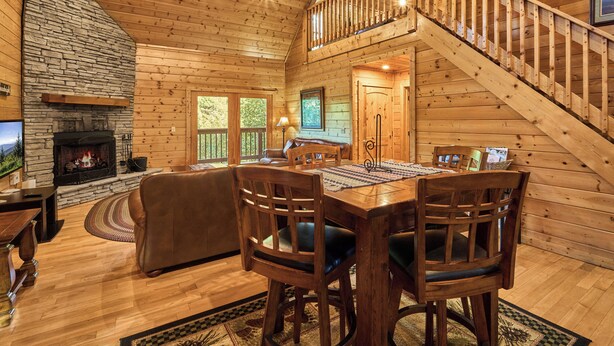 Interior de una cabaña de madera con chimenea, comedor y escalera.