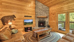 Interior acogedor de una cabaña con chimenea, sofás de cuero, televisor y una decoración de osos en la pared.