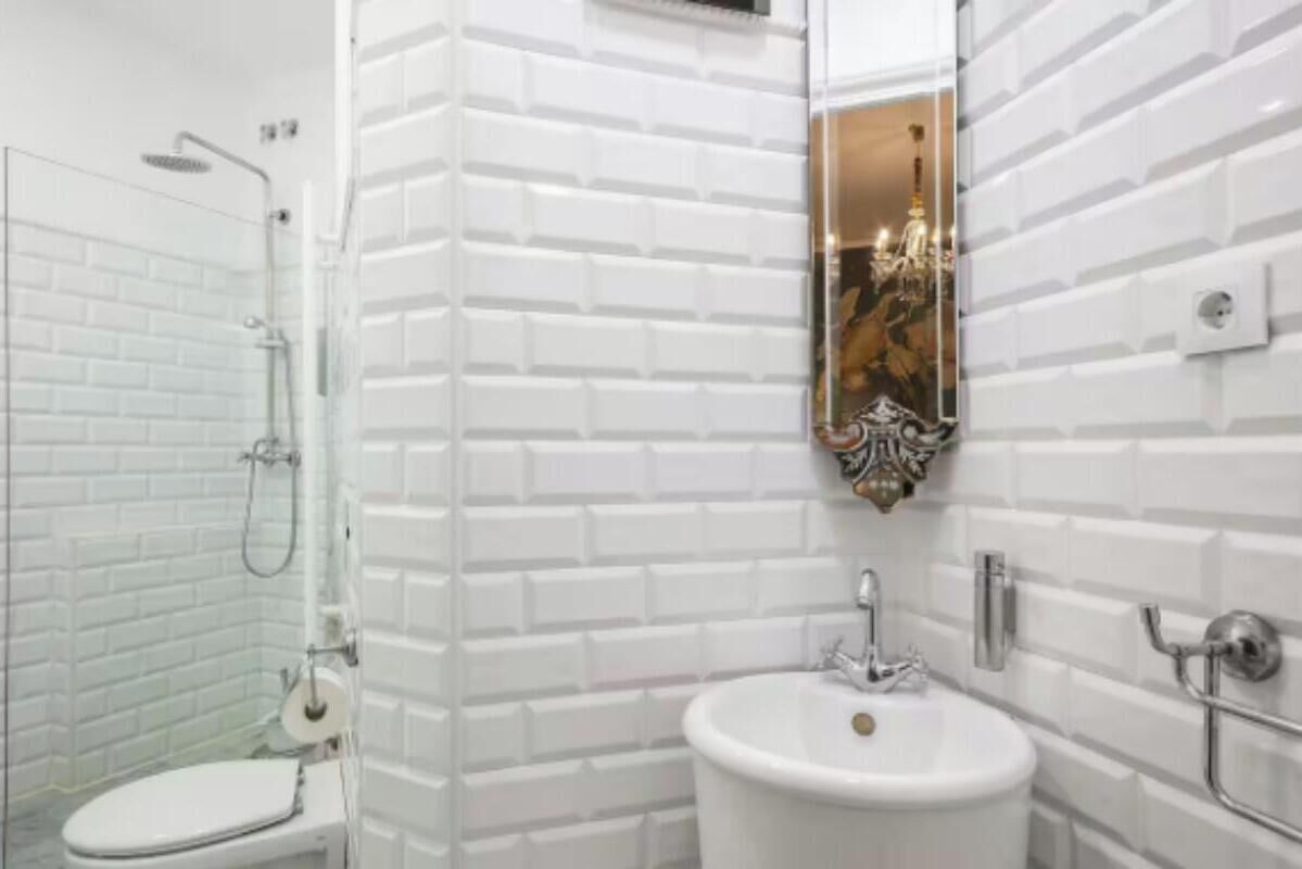 Un baño con paredes de azulejos tipo metro blancos, un lavamanos blanco y una ducha.