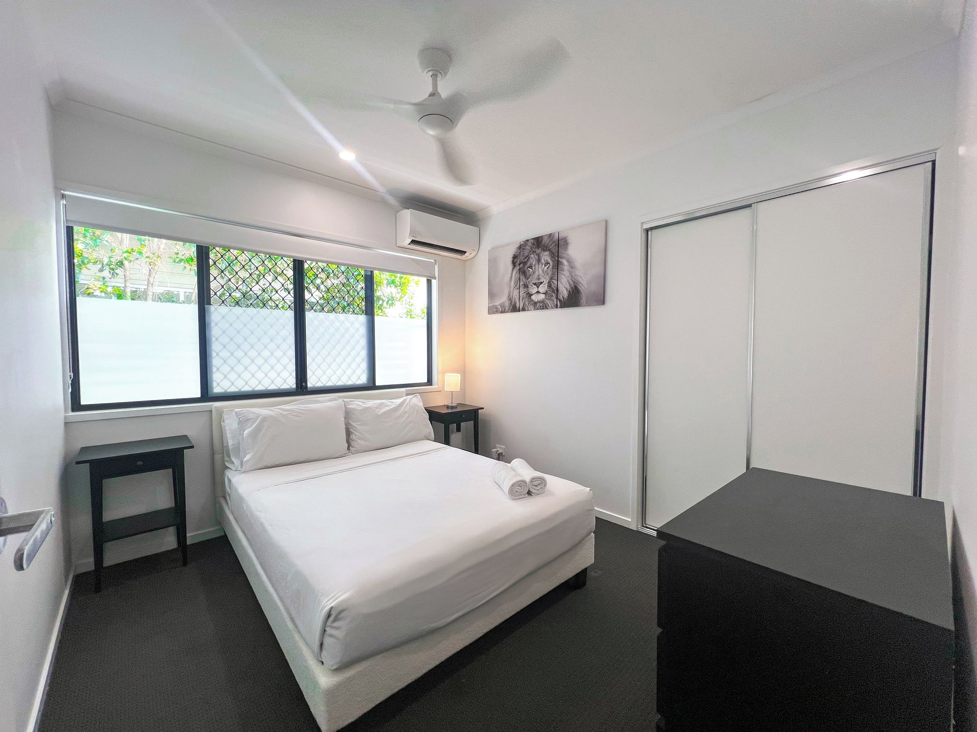 A bedroom with a bed, a nightstand, a window with a view, a ceiling fan, and a wardrobe.