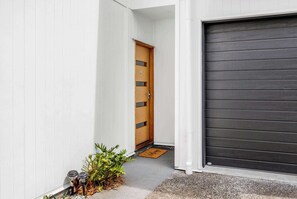 A modern house with a wooden door, a dark garage door, and a small garden with plants and a welcome mat.