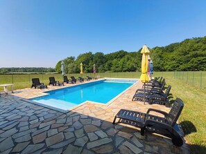 A rectangular swimming pool with a stone deck, surrounded by lounge chairs and umbrellas.