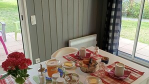 Ein Esstisch, reichhaltig gedeckt mit Frühstücksleckereien, eine Blumenvase und zwei an der Wand befestigte Hahnschmuckstücke.