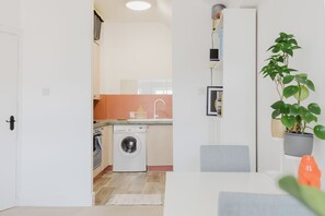 Eine kompakte Küche mit Waschmaschine, ein Essbereich mit Tisch und Stühlen sowie ein Blumentopf.