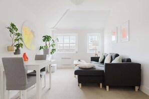 A modern living room with a white table, grey sofa, and potted plants. - Homely 1BD East London Hideaway (Greater London)