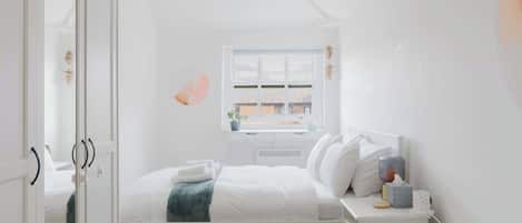 Un dormitorio con cama, mesita de noche, armario, ventana y vistas al exterior.