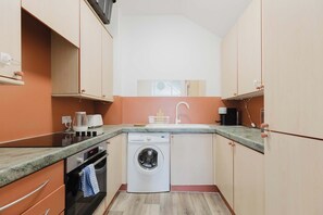 A compact kitchen with a washing machine, a coffee maker, and a microwave. - Homely 1BD East London Hideaway (Greater London)