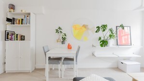 Une pièce moderne avec un bureau blanc, des chaises, une bibliothèque, une plante en pot et un tableau encadré au mur.