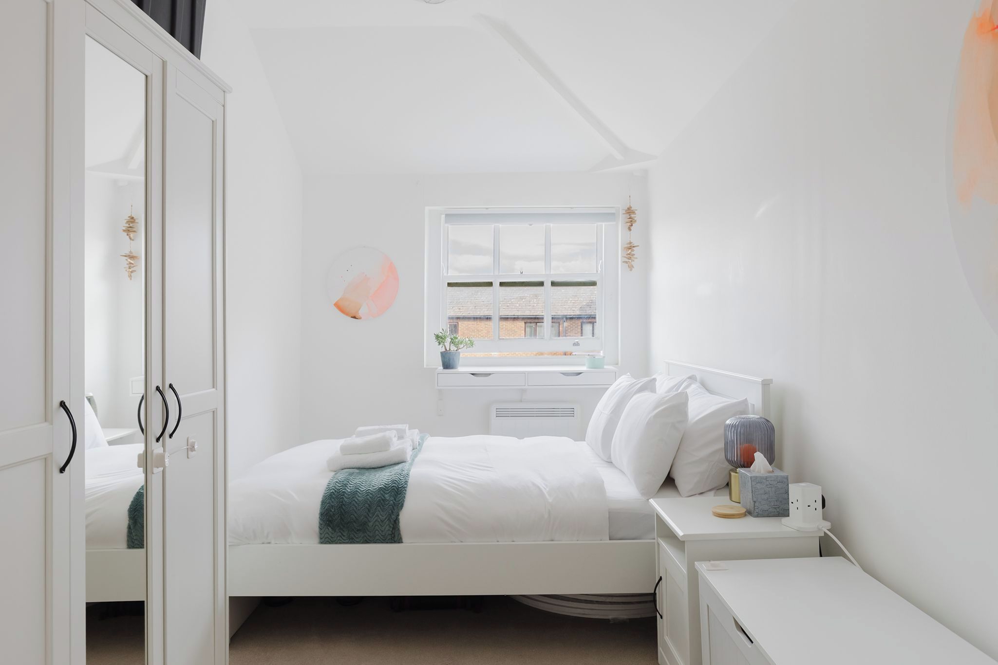 A minimalist bedroom with a bed, bedside table, and a window with a view of buildings.
