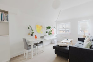 Un salon moderne avec un canapé blanc, une table à manger avec des chaises, une bibliothèque et deux fenêtres avec des rideaux.