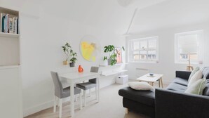 Un salon moderne avec une table à manger blanche, des chaises grises, un canapé noir et une bibliothèque.