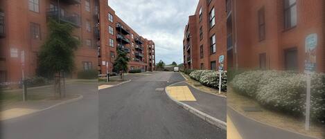 A street view of a residential area with brick apartment buildings, a clear sky, and a sign indicating a property for sale.