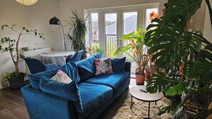 A living room with a blue sofa, a round table, and various potted plants.