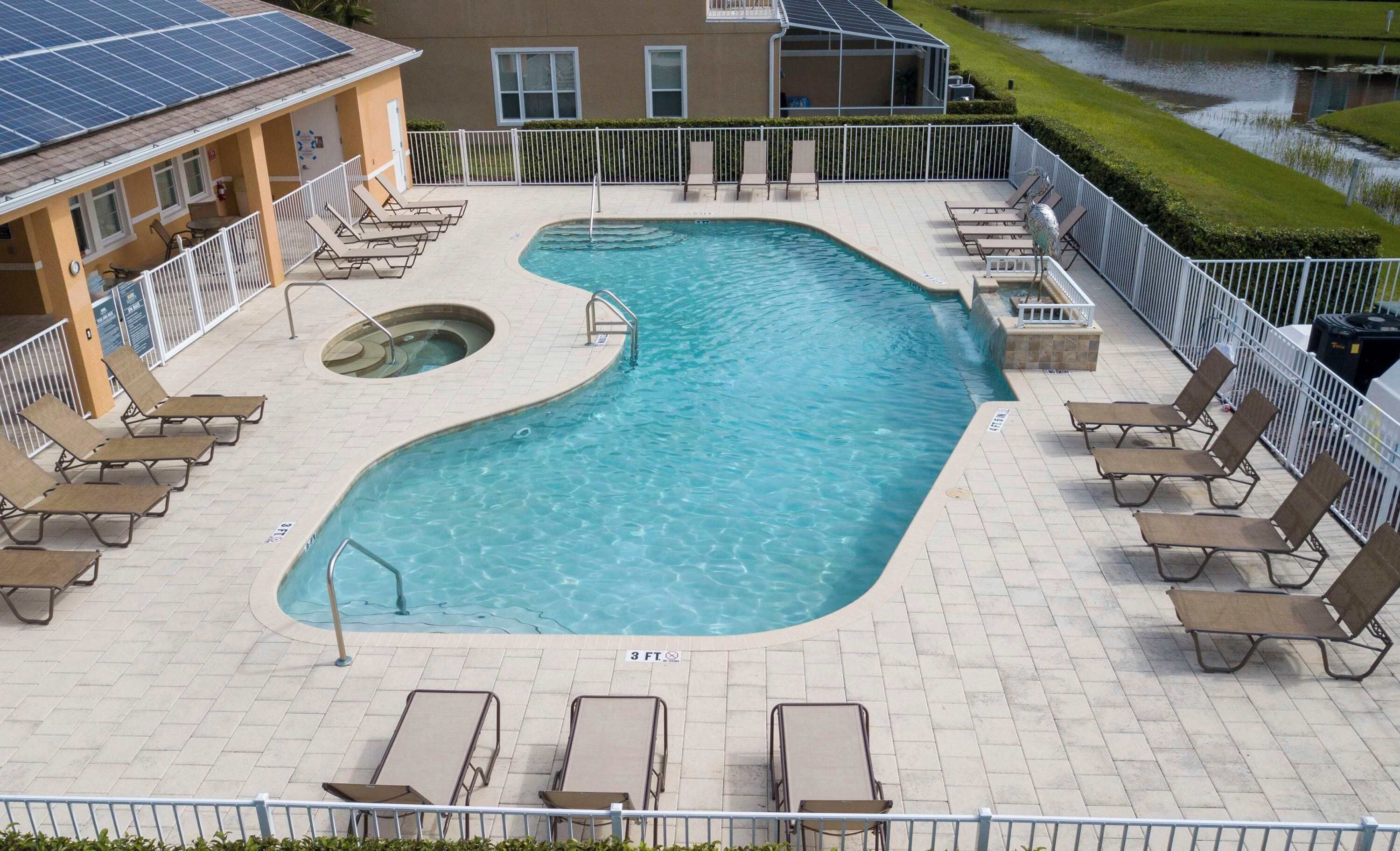 A swimming pool with a hot tub, surrounded by lounge chairs and a covered area with solar panels.