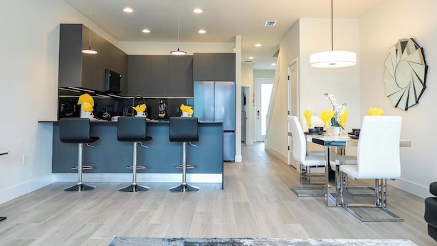 A modern kitchen with a central island, bar stools, and a dining area with a table and chairs. - Modern 3Bd Screened Pool at Serenity Resort 17322 (Clermont)