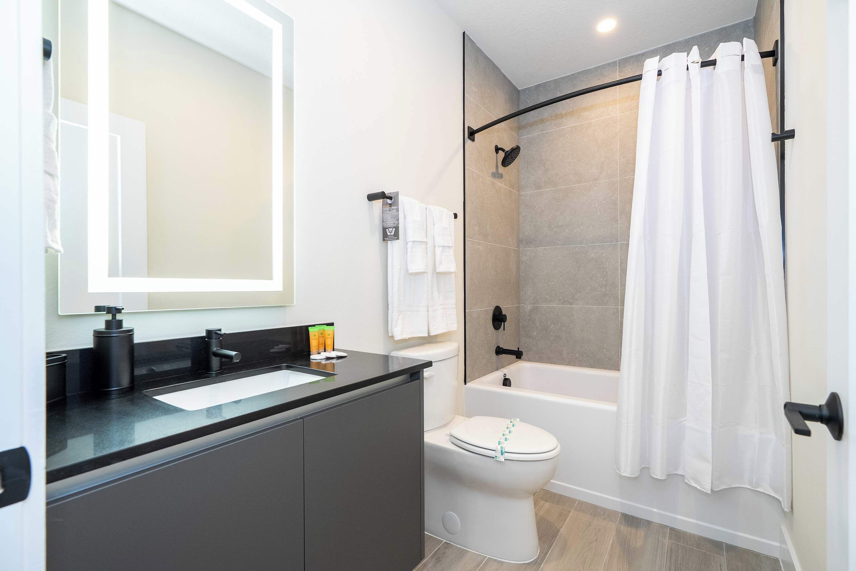 Un baño moderno con encimera negra, lavabo blanco y cabina de ducha con paredes de vidrio.
