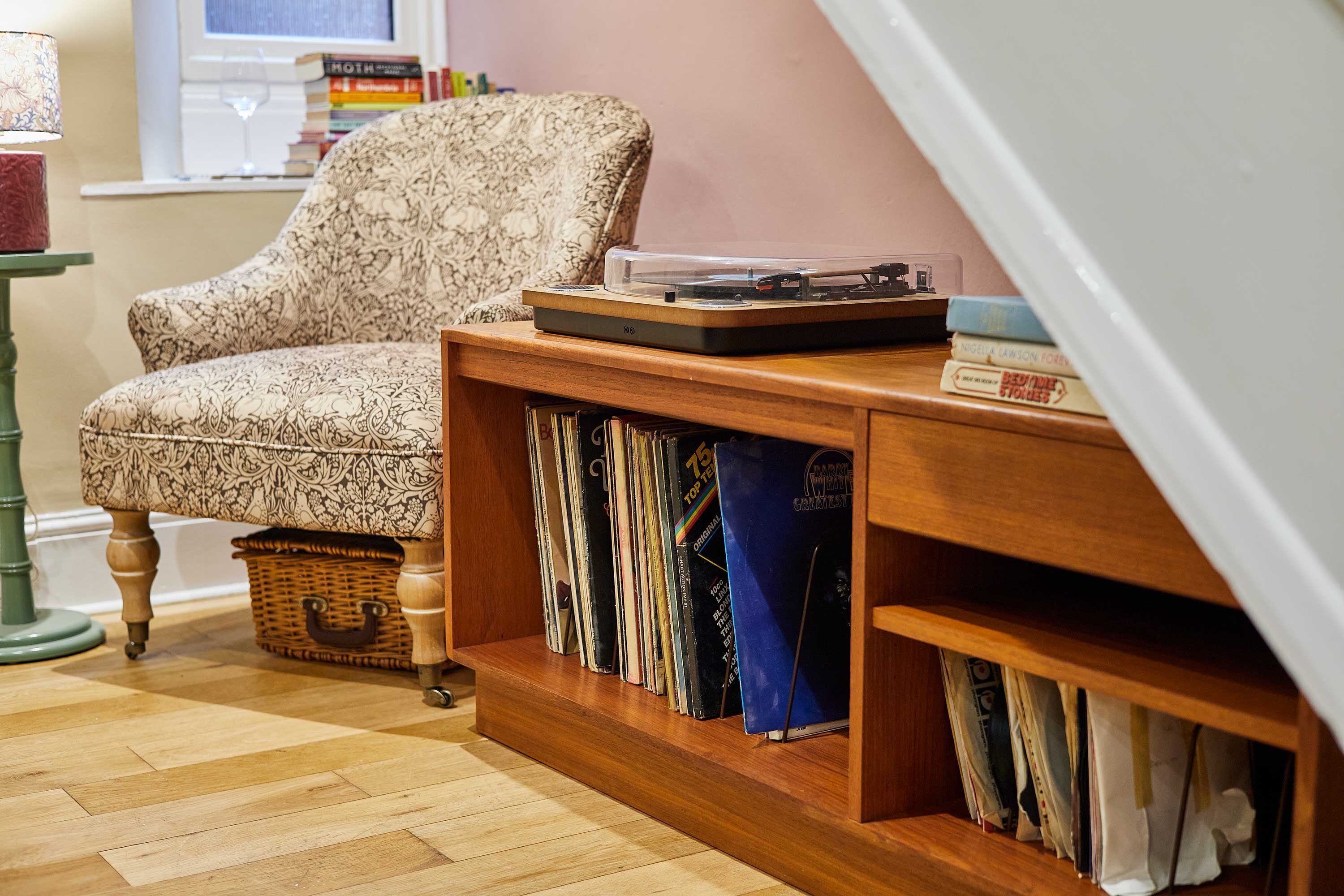 Un coin lecture confortable, avec un fauteuil à motifs, une petite table en bois sur laquelle est posé un tourne-disque, et une bibliothèque remplie de livres.