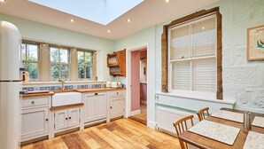 A kitchen with wooden flooring, white cabinets, a dining table with chairs, and a window with shutters. - Host Stay Sonsy Cottage (Alnwick)
