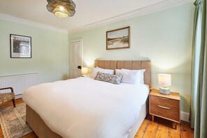 A hotel room with a large bed, a nightstand with a lamp, a framed picture on the wall, and a window with curtains. - Host Stay Sonsy Cottage (Alnwick)