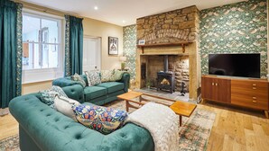 A living room with a stone fireplace, green sofas, a television, and a patterned wall. - Host Stay Sonsy Cottage (Alnwick)