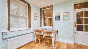 A dining area with a table set for two, wooden chairs, a white radiator, and a window with blinds. - Host Stay Sonsy Cottage (Alnwick)