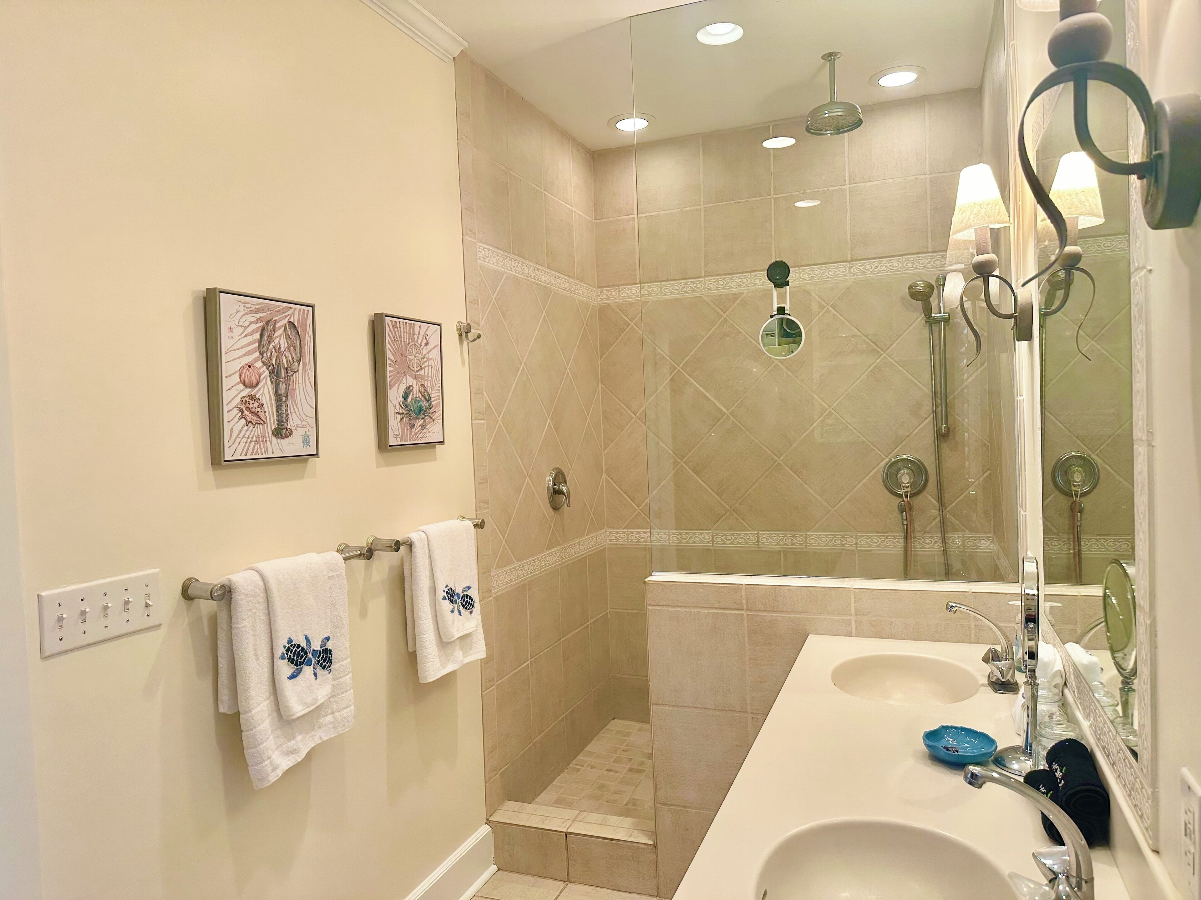 Ein Badezimmer mit Dusche, zwei Waschbecken und dekorativen Wandbildern.