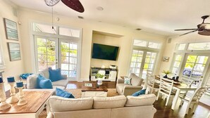 Un salon spacieux avec un grand canapé, une table basse en bois et un coin repas comprenant des chaises et une table blanches.