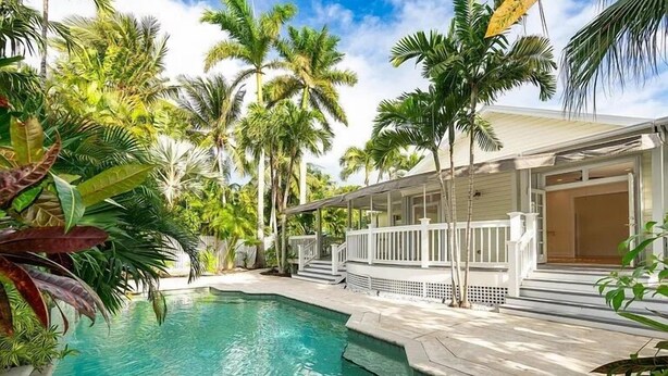 Une piscine entourée de palmiers et une terrasse couverte.