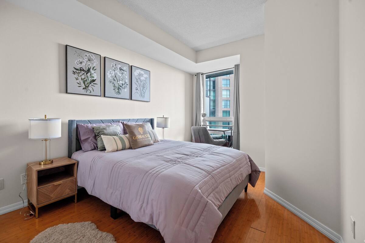 A bedroom with a bed, bedside tables, a nightstand, a lamp, and a window with curtains.