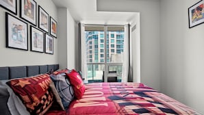 A bedroom with a large bed, a window with curtains, and framed pictures on the wall. - Atlantis at Waterpark City Condos in DT (Toronto)
