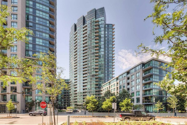 A high-rise building with multiple balconies, surrounded by trees and other modern buildings. - Atlantis at Waterpark City Condos in DT (Toronto)