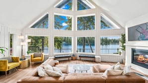 Ein geräumiges Wohnzimmer mit hoher Decke und großen Fenstern mit Blick auf einen See.