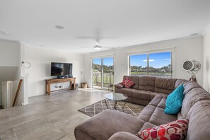 A spacious living room with a large sectional sofa, a glass coffee table, and a flat-screen TV on a wooden console. - Beach House on Longridge (Cowes)