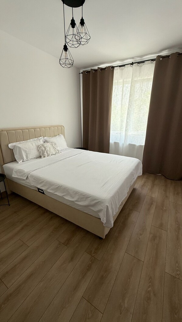 A bedroom with a large bed, wooden flooring, a headboard, and a hanging light fixture.