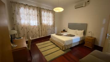 Ein Hotelzimmer mit Bett, Nachttischen, Schreibtisch, Sessel, Lampe, Teppich und einem fensterbepflanzten Fenster.
