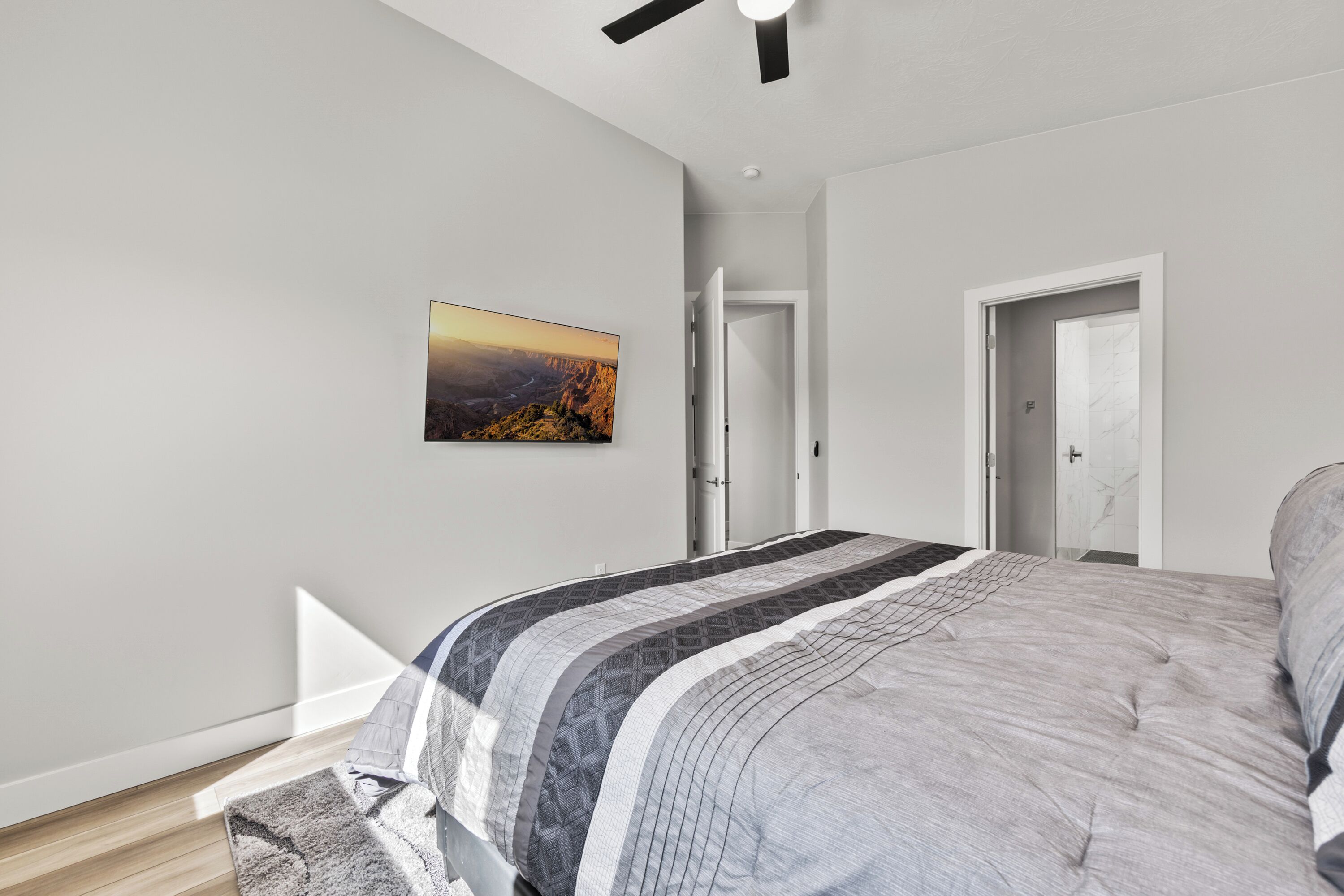 A modern bedroom with a large bed, a ceiling fan, and a painting on the wall.