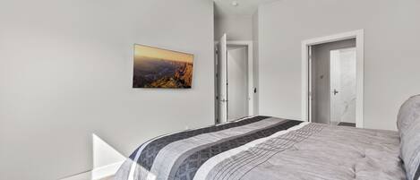 A modern bedroom with a large bed, a ceiling fan, and a painting on the wall.