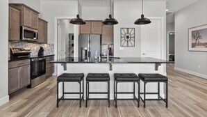 Une cuisine moderne dotée d’un îlot central, d’appareils électroménagers en acier inoxydable et de tabourets de bar noirs.