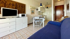 A compact room with a bed, a TV, a microwave, and a kitchenette. - Bright Seaview Apartment (Caorle)