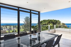 Ein moderner Essbereich mit Glastisch und Stühlen, der einen malerischen Blick auf das Meer und viel Grün bietet.