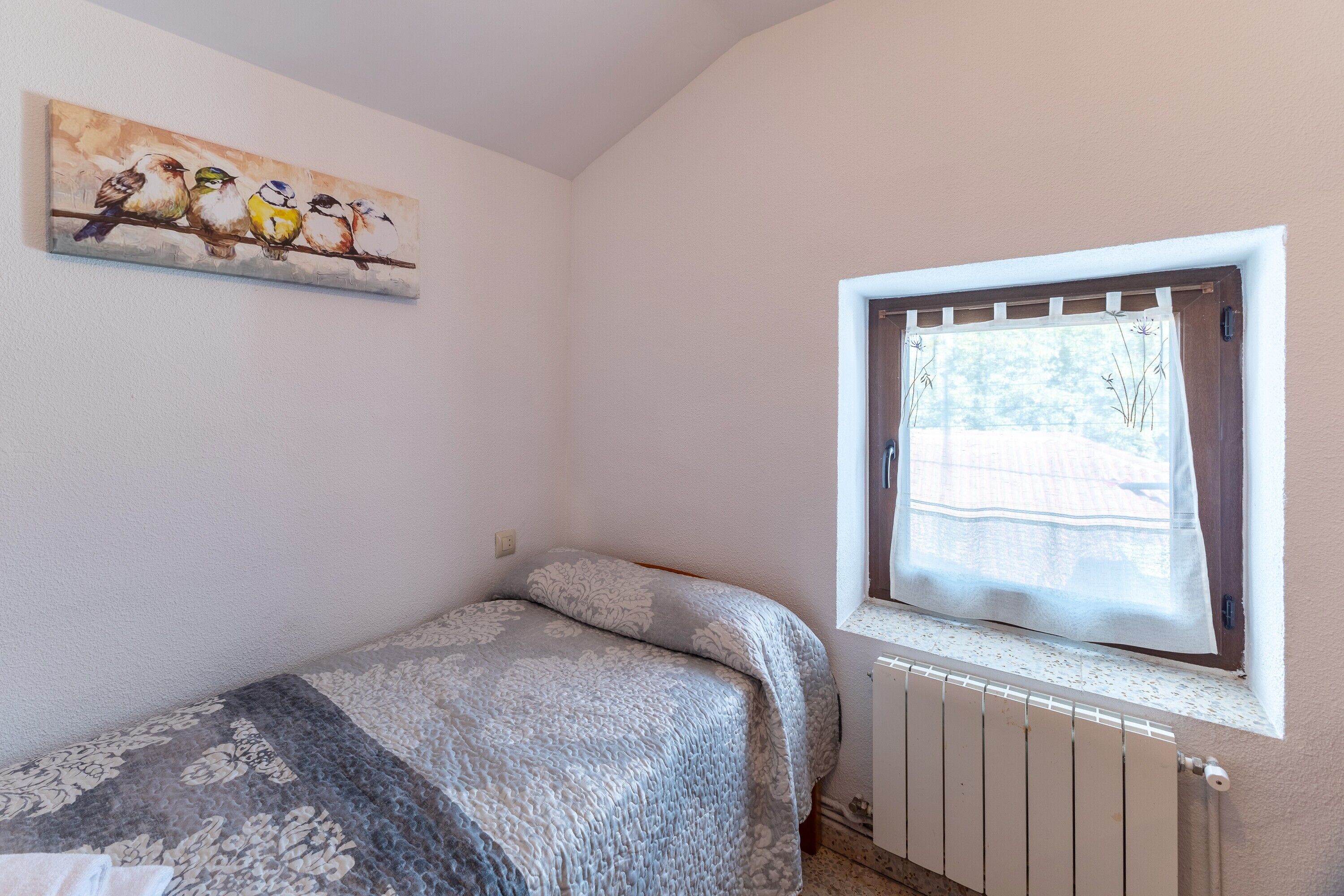 A bedroom with a bed, a window with a view, and a painting on the wall.