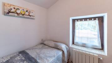 A bedroom with a bed, a window with a view, and a painting on the wall.