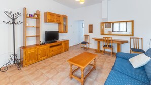 Ett vardagsrum med en TV, trämöbler, en soffa och en matplats.