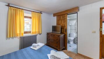 Un dormitorio con una cama, un aparador, un televisor y un baño visible a través de una puerta abierta.