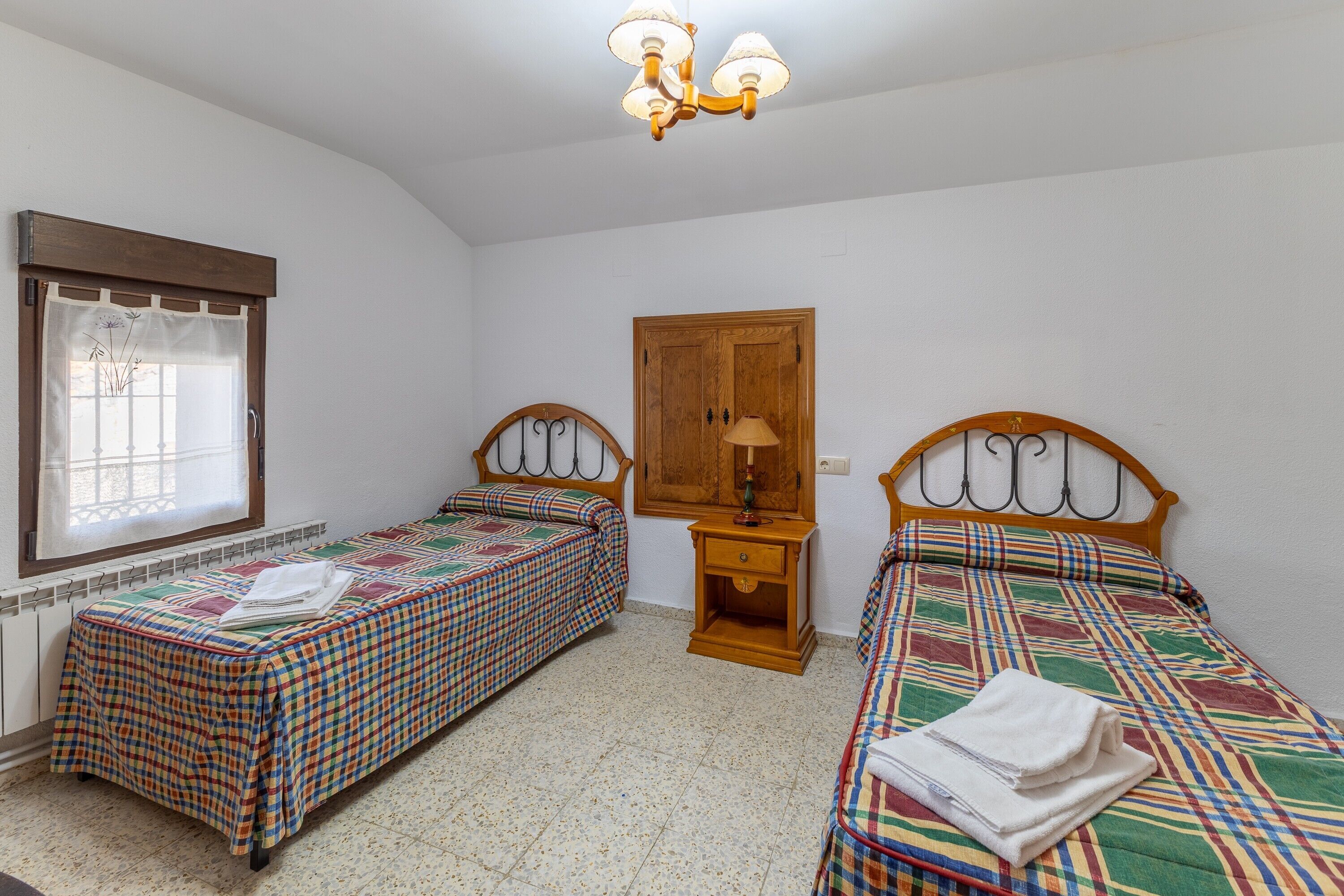 Una habitación con dos camas individuales, un armario de madera, una mesita pequeña y una ventana con cortinas.