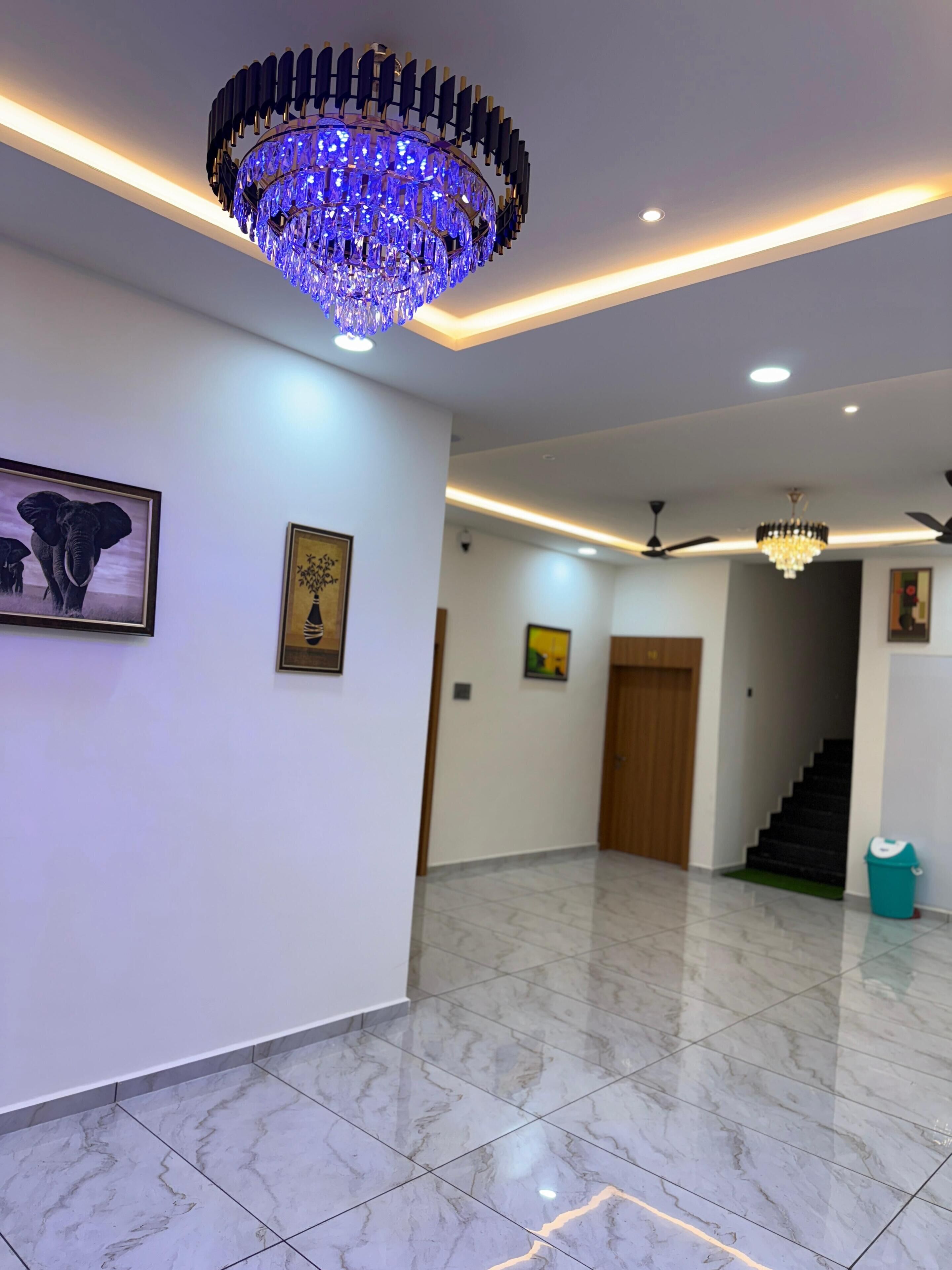 A spacious hallway with marble flooring, a large chandelier, ceiling fans, and framed artwork on the walls.